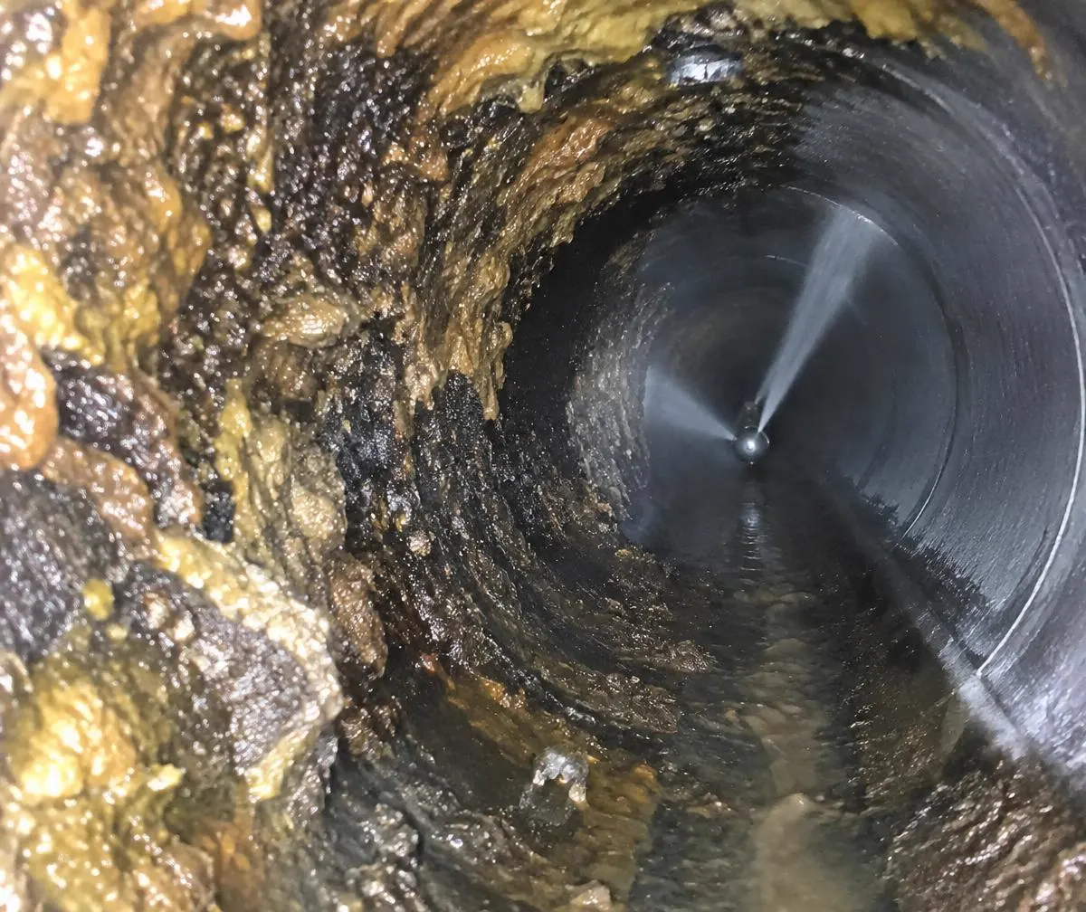 Grease and scale inside a pipe being cleared by a jetting nozzle