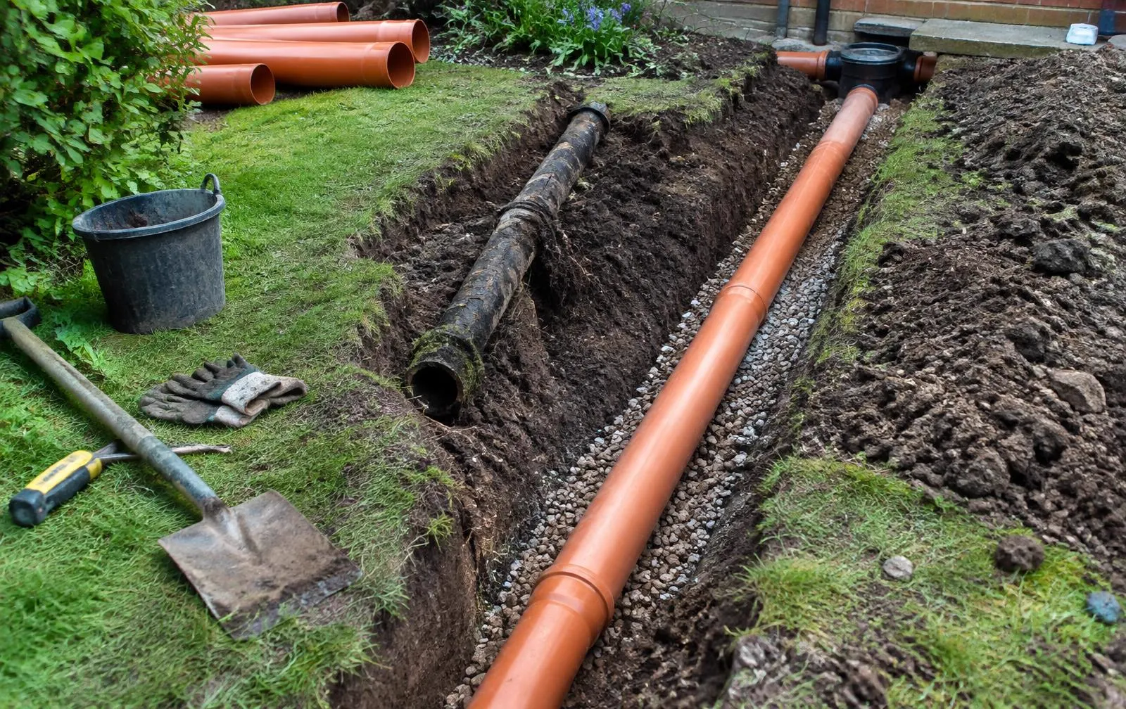 Old pitch fibre pipe beside new plastic drain pipe in a trench